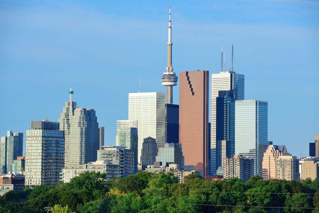 image | Manage Your Property Toronto skyline featuring the CN Tower and surrounding glass high-rises against a clear blue sky.